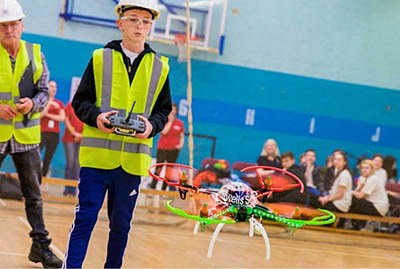 Child using a remote control to move a model helicopter around a school hall.